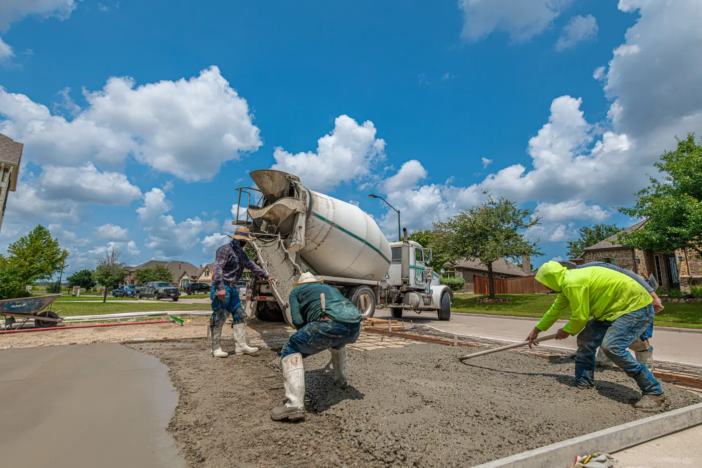 A concrete crew placing and screeding a residential slab as the mixer truck discharges