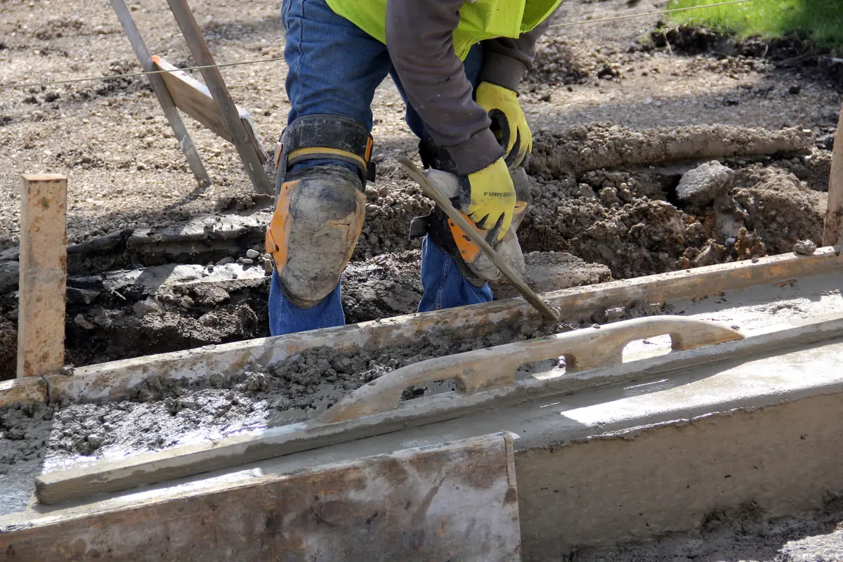 A concrete driveway edge formed and hand-finished beside broken-out slab sections