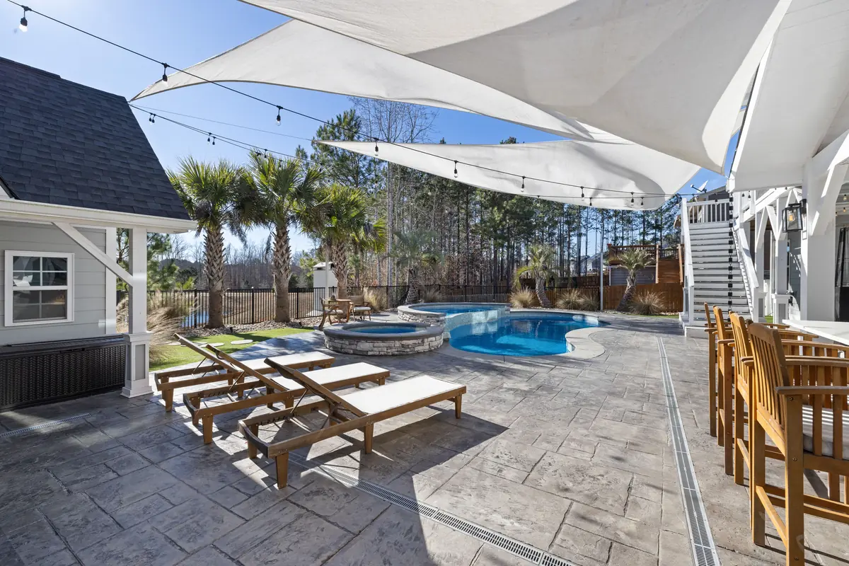 A concrete pool deck with loungers and shade sails over the surface