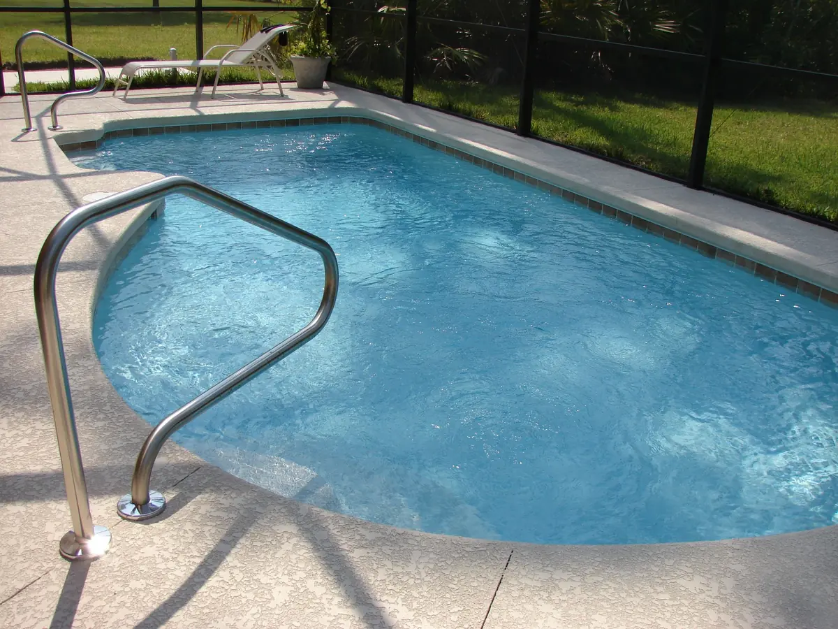 A textured concrete pool deck running around the edge of a swimming pool